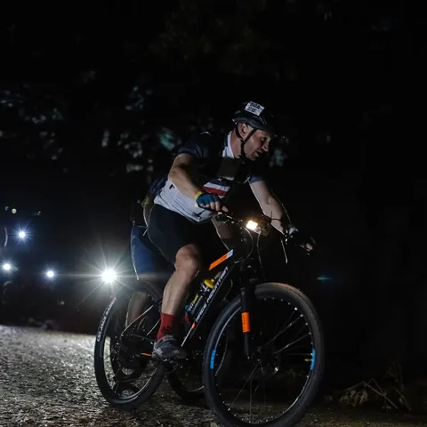 A mountain biker riding through the night under a headlamp.