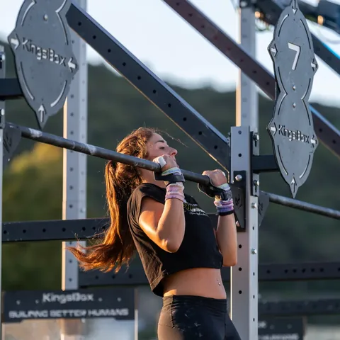 An athlete resting on the bar of a pull-up rig between reps.